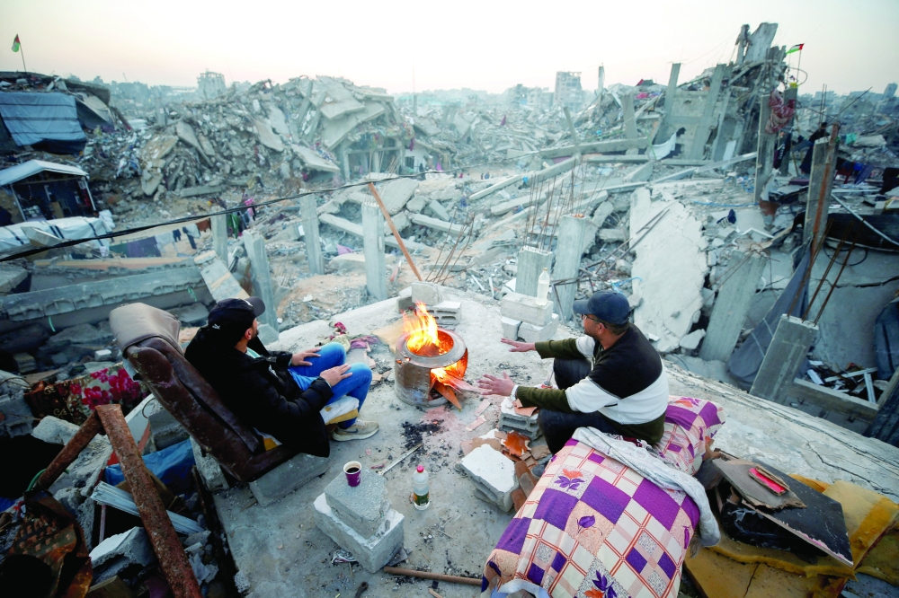 Palestinians sit next to a fire among the rubble of buildings destroyed during the Israeli offensive, northern Gaza. — Reuters