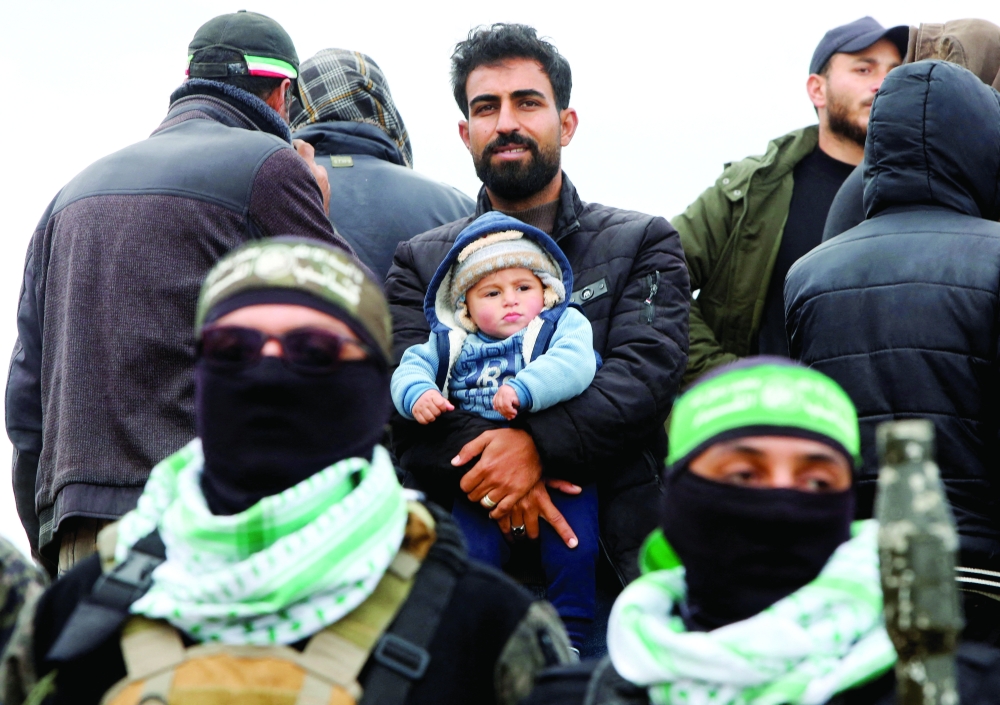 A Palestinian man with a child looks on as Hamas soldiers stand guard in Khan Yunis. — Reuters