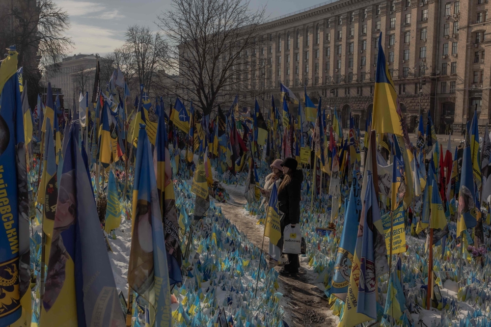 Visitors stand next to a makeshift memorial paying tribute to Ukrainian fighters with flags at the Independence Square in Kyiv. — AFP