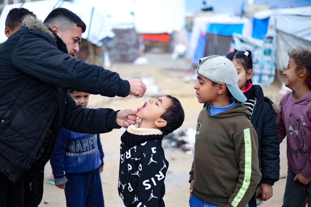 Children look on a Palestinian boy receives a polio vaccine at a camp for displaced people in Nuseirat. — AFP