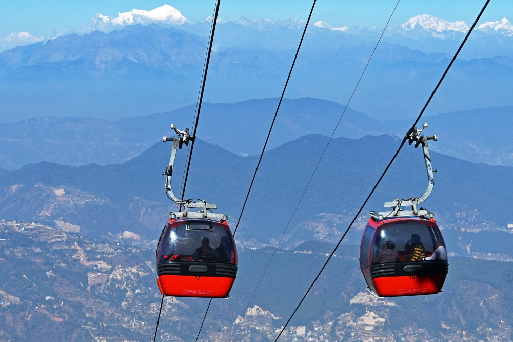 In this photograph taken on February 3, 2025, people ride cable cars over the Chandragiri hilltop, on outskirts of Kathmandu. They appear tranquil when soaring above Himalayan forests, but a string of cable car projects in Nepal have sparked violent protests with locals saying environmental protection should trump tourism development. (Photo by Prakash MATHEMA / AFP)
