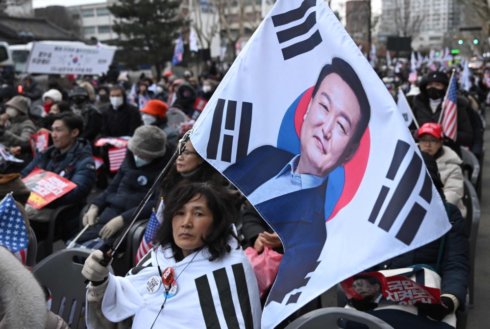 A supporter of South Korea President Yoon Suk Yeol waves a flag showing a picture of Yoon during a rally near the Constitutional Court in Seoul on February 25, 2025, as Yoon is scheduled to attend his final impeachment hearing. (Photo by Jung Yeon-je / AFP)