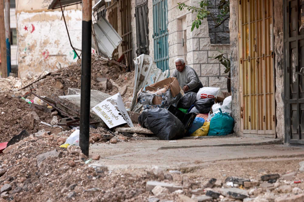 A man removes dirt and debris piled up in front of his residence along a street destroyed by Israeli bulldozers, during an ongoing military raid in the occupied West Bank refugee camp of Tulkarem.— AFP 