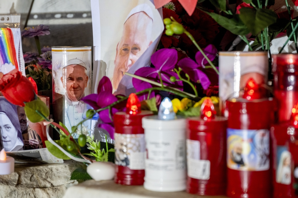 Flowers and candles at the base of the statue of Pope John Paul II outside Gemelli Hospital in Rome, where Pope Francis is being treated for pneumonia, Feb. 23, 2025. (James Hill/The New York Times)