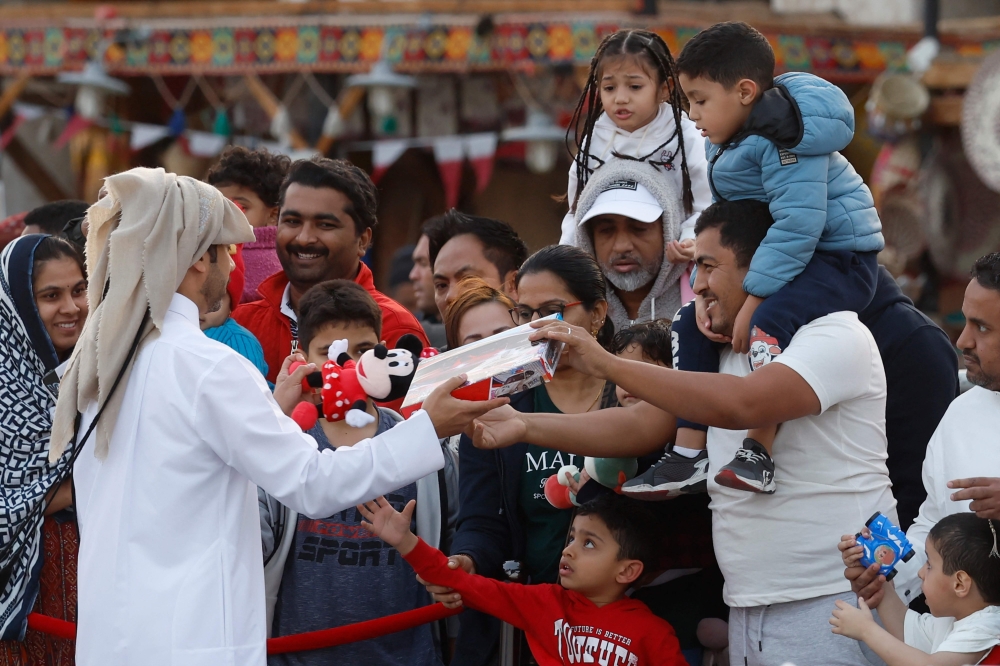A volunteer distributes children's toys during Ramadan to people on the first day of the holy month of Ramadan, at Souq Waqif in Doha on March 1, 2025. (Photo by KARIM JAAFAR / AFP)
