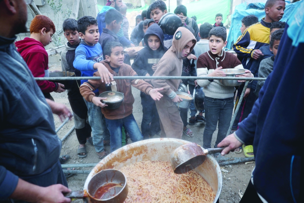Palestinian children wait for a meal during food distribution at a charity kitchen at the Nuseirat refugee camp. — AFP
