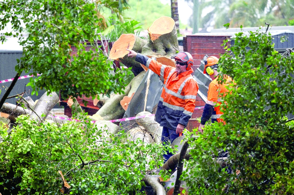 Workers cut up a fallen tree that damaged the fence of a house at Surfers Paradise on the Gold Coast. — AFP