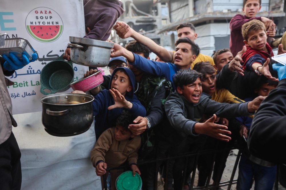 Displaced Palestinian children push into a queue to get a portion of cooked food from a charity kitchen in Beit Lahia in the northern Gaza Strip. — AFP