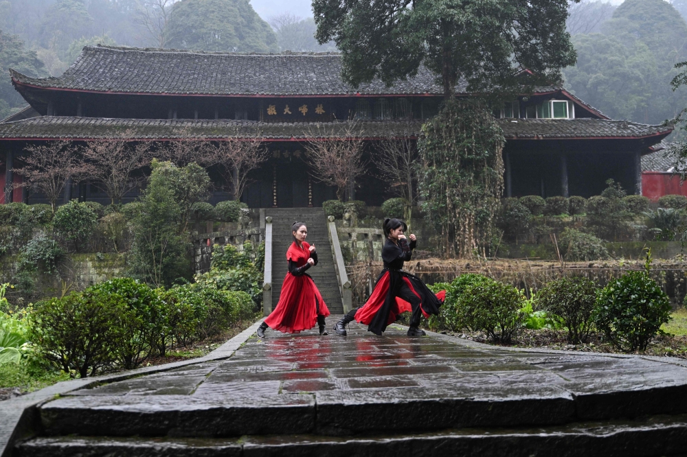 This photo taken on February 21, 2025 shows Duan Ruru (L), a founding member of the Emei Kung Fu Girls, and Liu Qiao demonstrating their martial art movements at the Zhongfei temple in Emeishan, China's southwestern Sichuan province. The ancient Emei school in the mountains of Sichuan is thought to have welcomed a higher proportion of women and girls, but has struggled in recent years to raise its profile. That is now changing thanks to a group of women from Generation Z, who mesh skilful swordwork with social media smarts to help put the sect back on the map.
 - To go with 'CHINA-WOMEN-KUNG FU, FOCUS' by Mary YANG
 (Photo by ADEK BERRY / AFP) / To go with 'CHINA-WOMEN-KUNG FU, FOCUS' by Mary YANG

