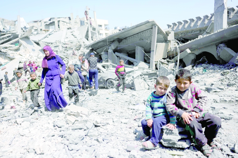 Children look on as people walk amid the rubble of a building destroyed in an overnight Israeli strike in Jabalia. — AFP
