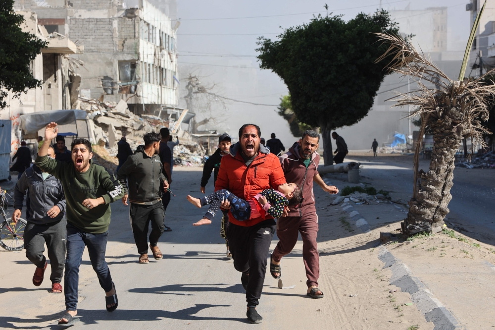 Palestinians rush an injured girl away from the site of Israeli strikes on a makeshift displacement camp in central Gaza City on Sunday. - AFP