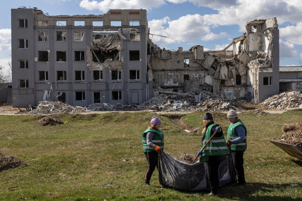 Municipal employees clean an area in front of a building which was heavily damaged, in Kherson, Ukraine. — Reuters