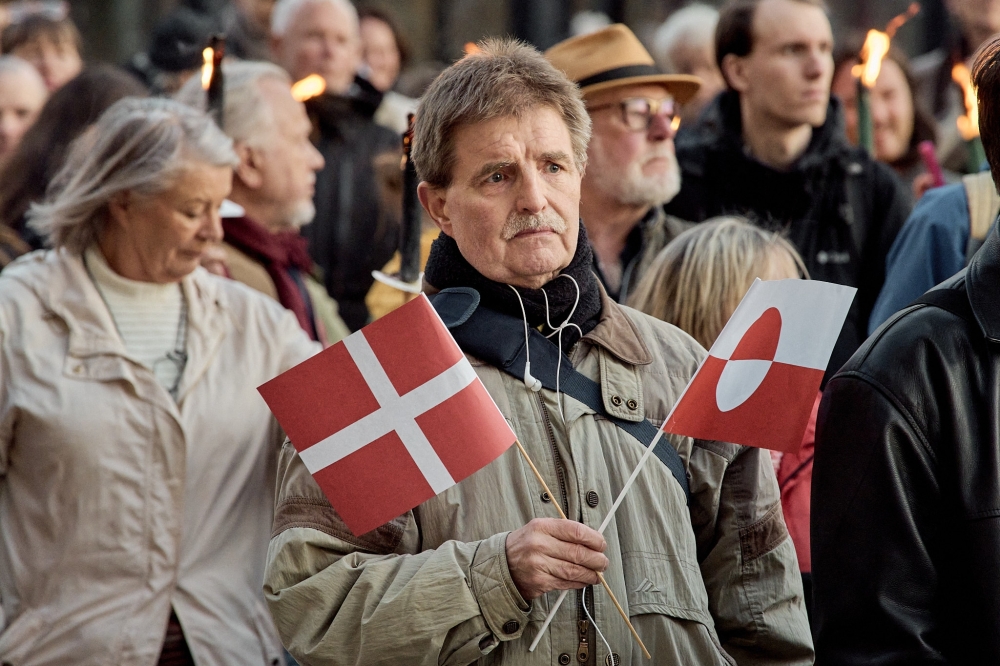 A man holds a Denmark and Greenland flag during a demonstration in support of Greenland, Copenhagen. — AFP