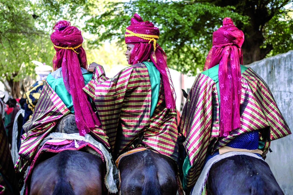 A horseman helps another one arrange his costume as they ride their horses before the Durbar. — AFP