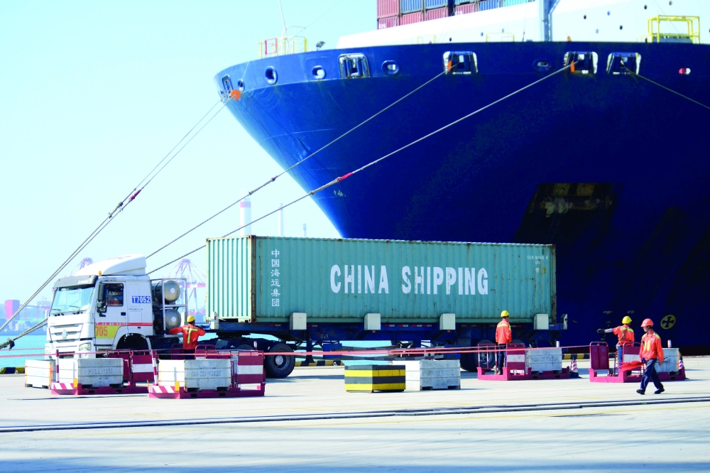 A truck transports a container next to a cargo vessel at a port in Qingdao, Shandong province, China. — Reuters