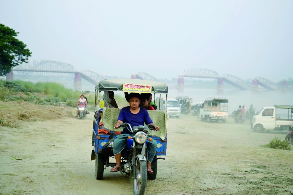 A driver transports people on the banks of the Irrawaddy River in front of the collapsed Ava Bridge, also known as the Inwa Bridge, in Sagaing, Myanmar. — AFP