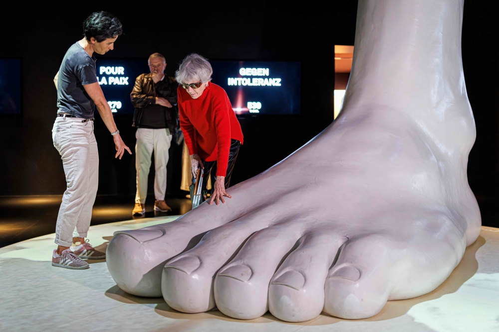 Waltraud Quiblier (R) touches a sculpture of a giant foot next to her image whisperer Cecile Crassier Mokdad (L) as they take part in a guided tour for visually impaired people at the International Red Cross and Red Crescent Museum in Geneva. - AFP