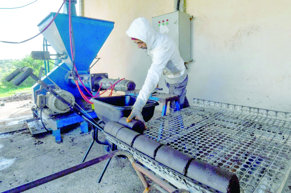 An employee operates a machine which turns olive pomace into heating briquettes, at the grounds of start-up Bioheat. - AFP