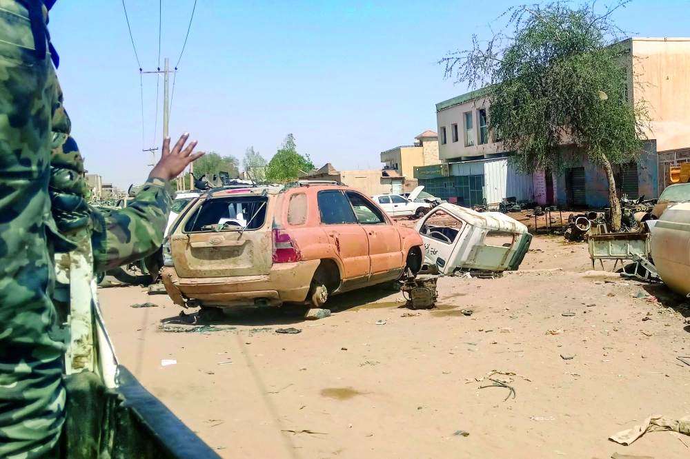 A Sudanese army soldier gestures from the back of a vehicle as it drives past damaged cars, in Khartoum. — AFP
