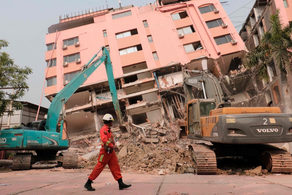 A rescue worker walks past heavy construction equipment being used to clear rubble at the site of a collapsed building in Mandalay. - AFP