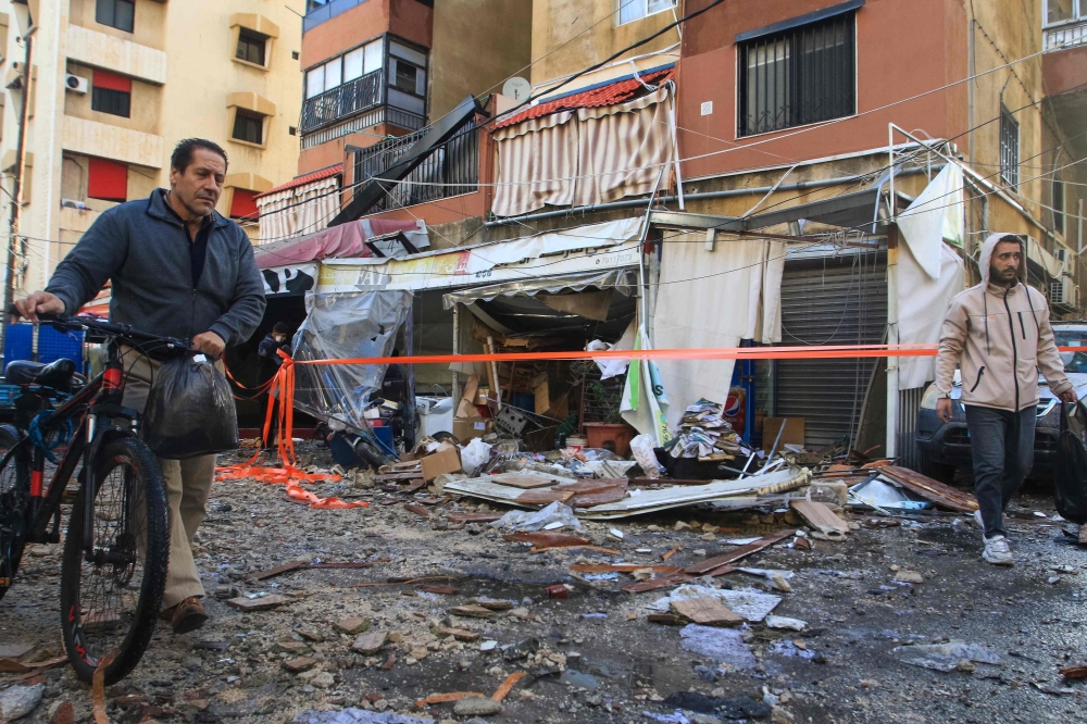 Local residents walk past debris in front of an apartment building following an Israeli strike in Sidon. — AFP