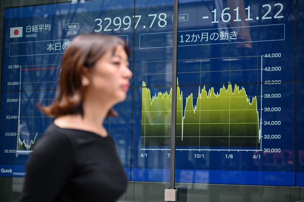 A pedestrian walks past an electronic board showing the morning numbers on the Tokyo Stock Exchange along a street in Tokyo. - AFP
