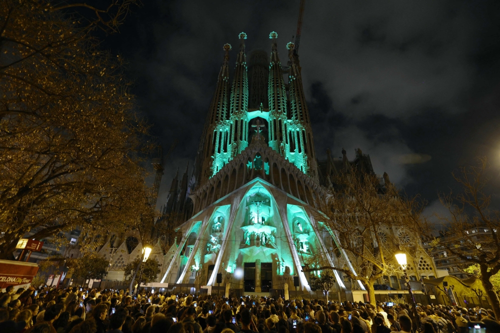 People watch a light show projected on the facade of Spanish architect Antoni Gaudi's Sagrada Familia Basilica, marking the start of the Holy Week, in Barcelona on April 14, 2025. The Catholic Church has put Antoni Gaudi, the designer of Barcelona's Sagrada Familia basilica nicknamed "God's architect", on the path to sainthood, the Vatican said today. Pope Francis recognised the Catalan architect's "heroic virtues" and authorised a decree declaring him "venerable", the Vatican said in a statement. (Photo by LLUIS GENE / AFP)


