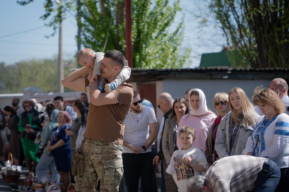 An Ukrainian serviceman carries his toodler during Easter service, in Kharkiv. — AFP