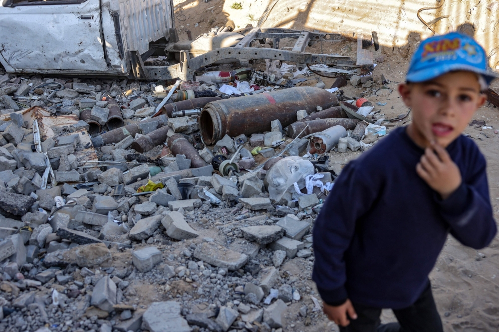A displaced Palestinian boy stands in front of unexploded ordnance near a police station-turned-shelter in Gaza City on Sunday. — AFP
