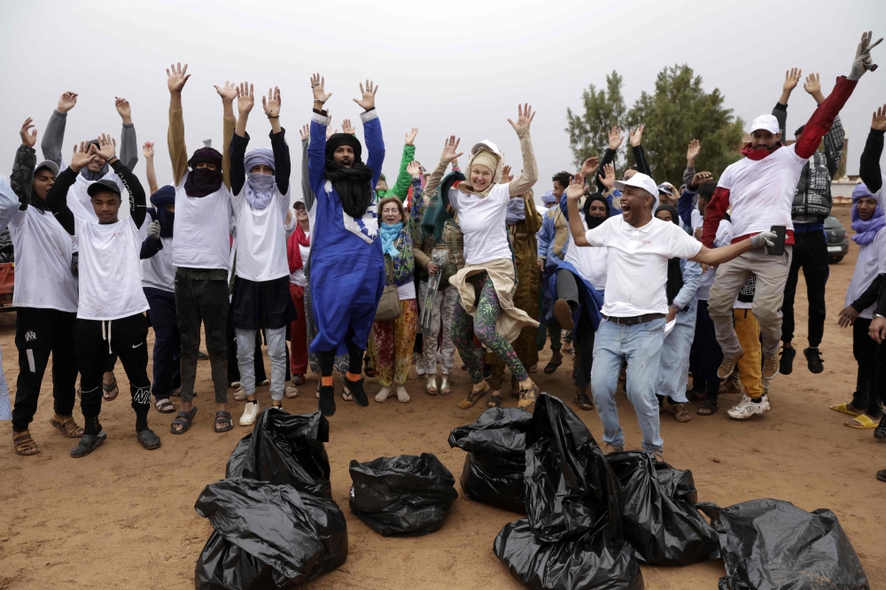 Volunteers, including tourists, cheer in front of bags of waste that they collected, after taking part in a desert cleaning campaign during the Nomads Festival in Mhamid El-Ghizlane in Morocco's southern Sahara desert on April 12, 2025. It may be the gateway to the vast Sahara desert, but that doesn't mean it's free of that modern scourge of the environment: the rubbish humanity discards. (Photo by Abdel Majid BZIOUAT / AFP)

