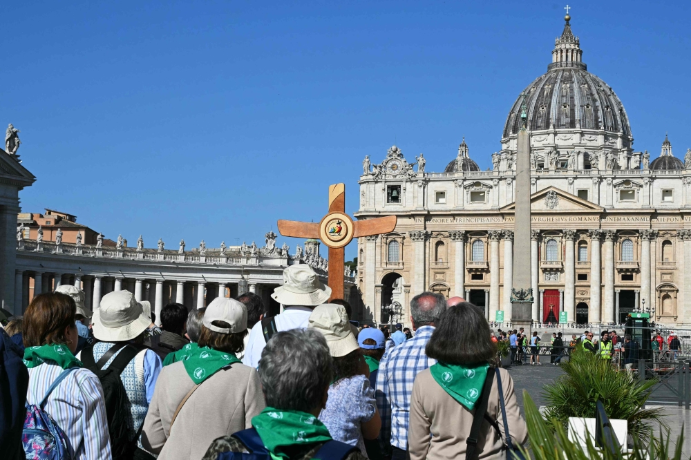 Pilgrims walk following a cross with St. Peter's basilica in the background at the Vatican, a day after the Pope's death, on April 22, 2025. The Pope died of a stroke, the Vatican announced hours after the death on April 21, 2025, of the 88-year-old reformer who inspired devotion but riled traditionalists during 12 years leading the Catholic Church. (Photo by Andreas SOLARO / AFP)

