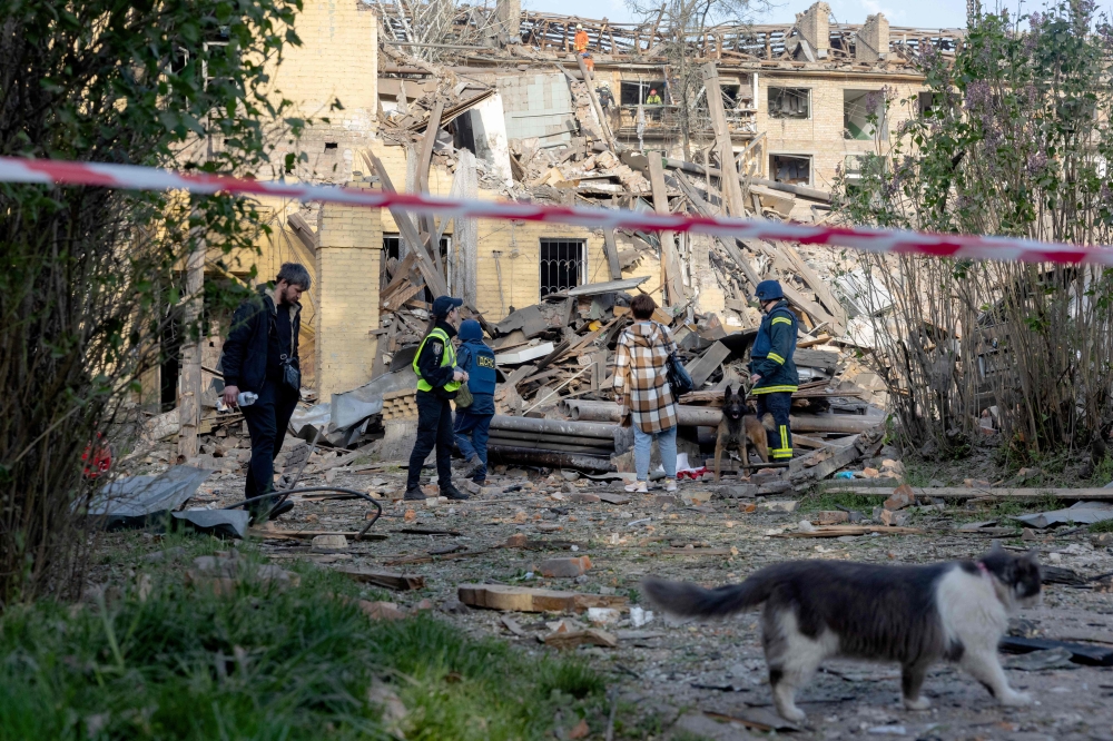 Police officers and local residents stand next to damaged apartment buildings following a Russian missile attack in Kyiv amid the Russian invasion of Ukraine. - AFP
