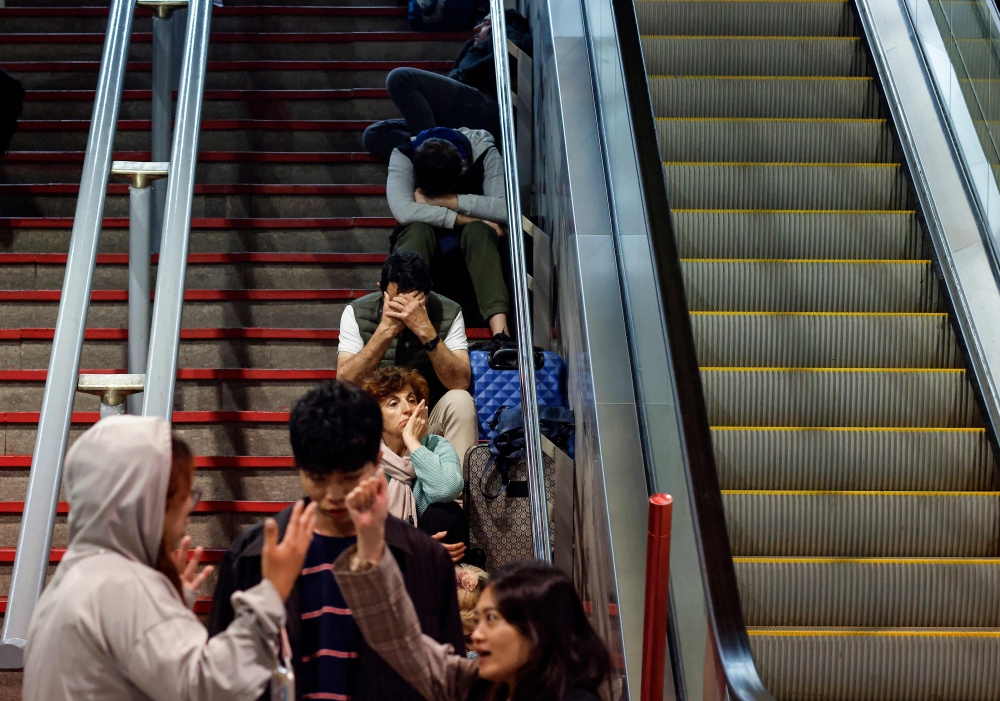 Travelers sit on the stairs as they prepare to spend the night at the Atocha train station, following a massive power cut affecting the entire Iberian peninsula and the south of France, in Madrid on April 28, 2025. Spanish Prime Minister Pedro Sanchez said today authoritie