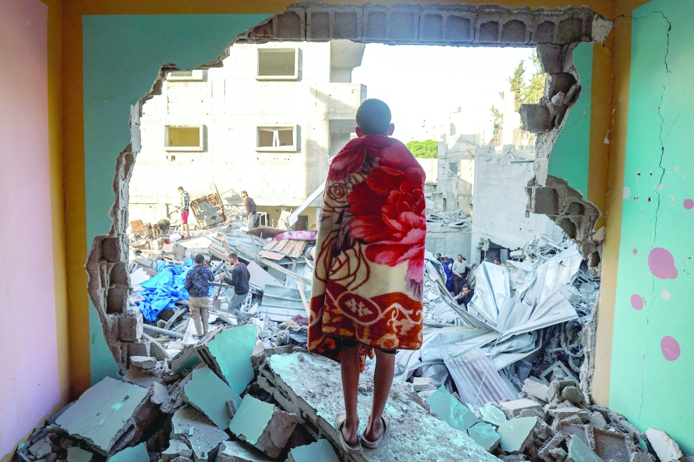 A youth draped in a blanket looks on as people look for survivors in the rubble of a building hit in an Israeli strike in the Bureij camp for Palestinian refugees in the central Gaza Strip on Friday. — AFP