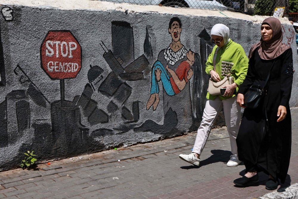 People walk past a wall a mural depicting destruction in the Gaza Strip in Ramallah in the occupied West Bank on Tuesday. - AFP