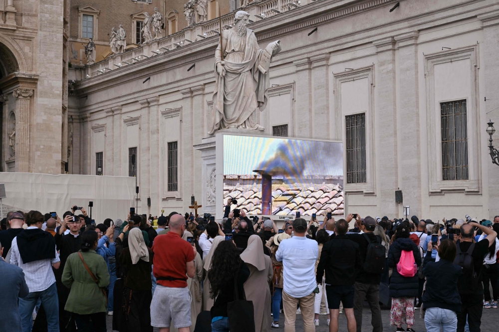 People watch a video screen after black smoke billowed from a chimney over the Sistine Chapel, in the Vatican. — AFP