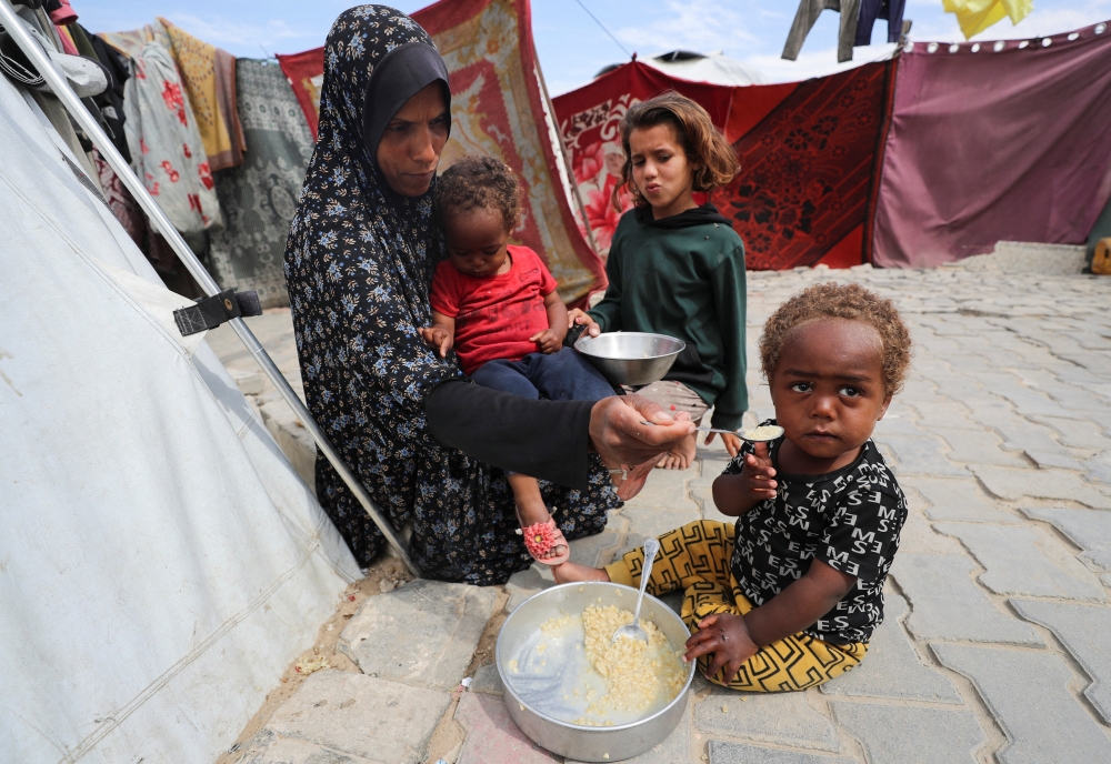 A Palestinian woman feeds her children in front of the tent that shelters them, in Gaza City. — Reuters