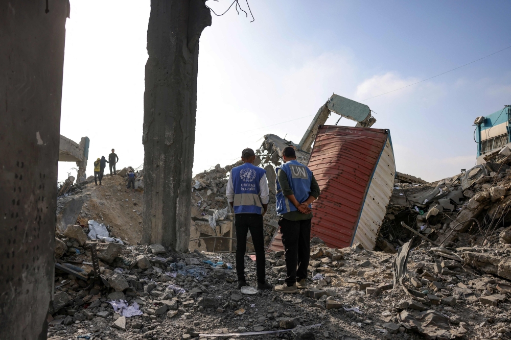 UN workers stand amid the rubble of an UNRWA school-turned-shelter, in Jabalia. — AFP