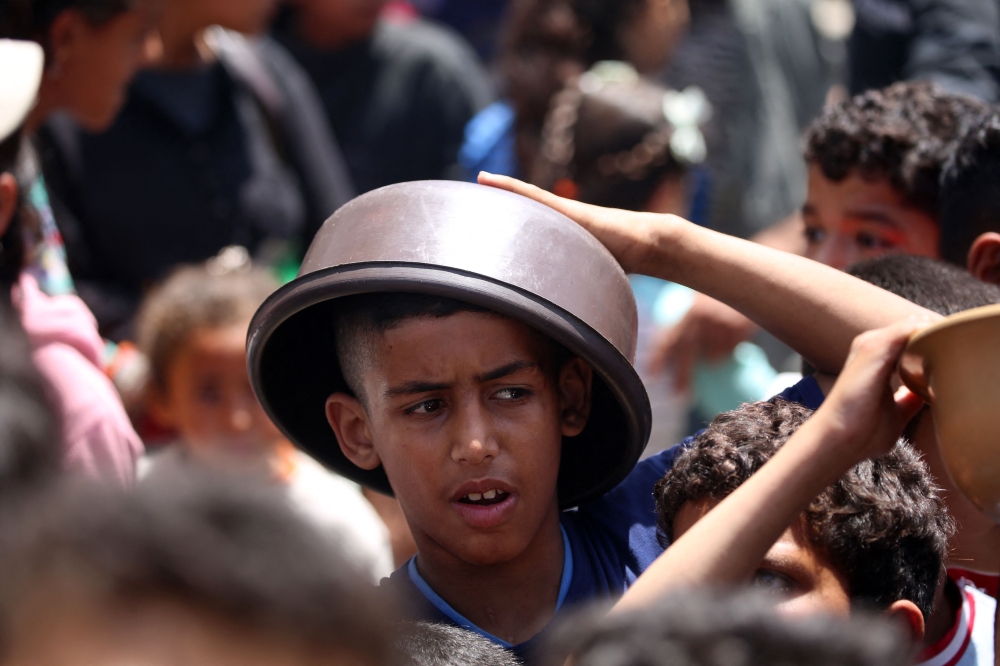 A Palestinian boy protects his head from the sun as he waits to get a hot meal, in front of a distribution point at the Nuseirat refugee camp in the central Gaza Strip on Saturday. - AFP