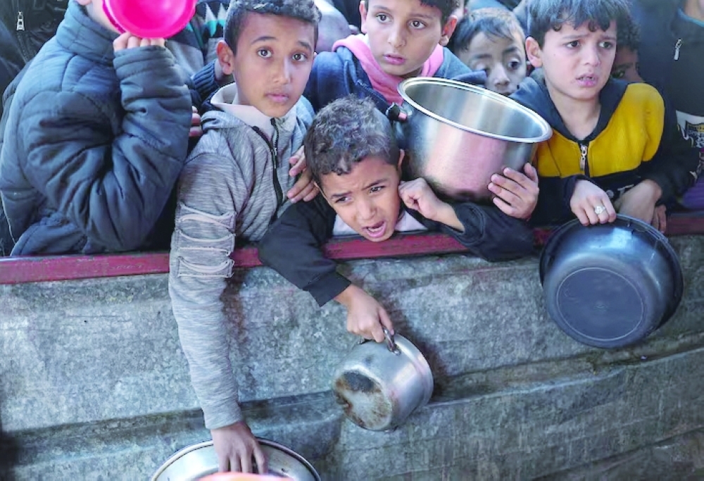 Palestinian children wait to receive food cooked by a charity kitchen amid shortages of food supplies in Rafah, in the southern Gaza Strip. - Reuters