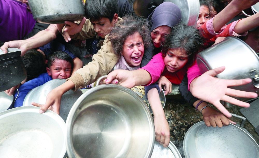 Palestinians wait to receive food cooked by a charity kitchen, in Jabalia. — Reuters