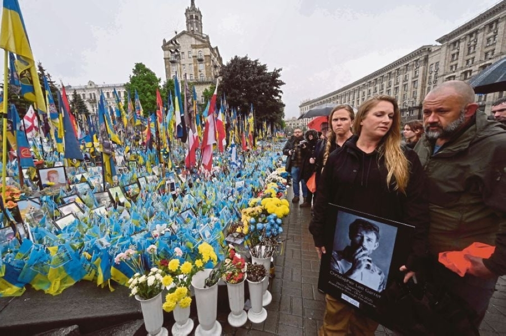 A woman holds a portrait at a makeshift memorial for the fallen Ukrainian and foreign fighters at Independence Square in Kyiv. - AFP