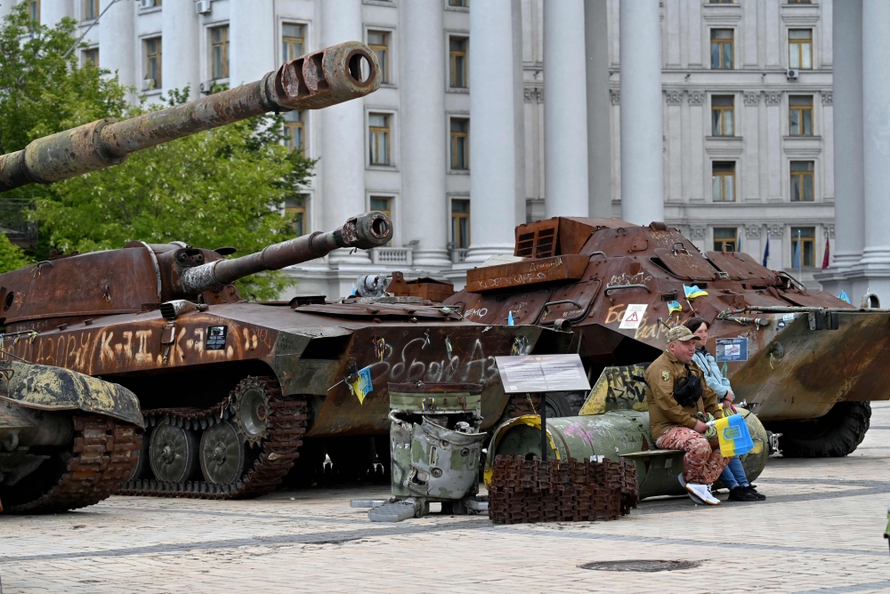 A volunteer sells Ukrainian flags as he sits on a fragment of a missile in the open-air museum in Kyiv on Tuesday. - AFP