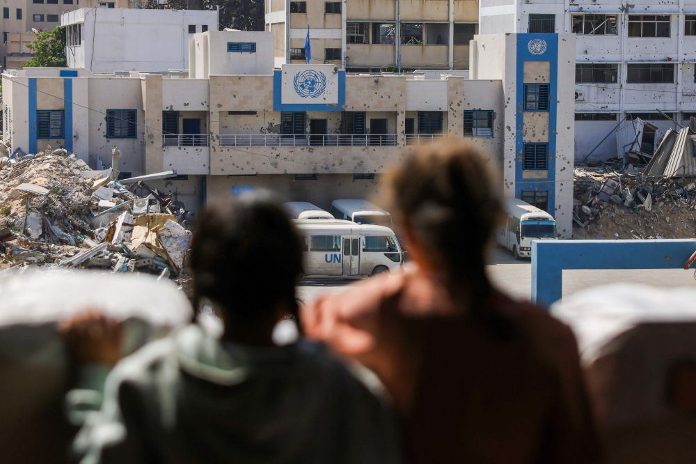 Children look at the closed UN agency for Palestinian refugees UNRWA headquarters in Gaza City, on May 20, 2025, amid the ongoing war between Israel and the Palestinian militant movement Hamas. Israel, pressing a newly expanded military offensive across the Gaza Strip, has faced mounting pressure including from key backer the United States to end the aid blockade it imposed on March 2. (Photo by Bashar TALEB / AFP)

