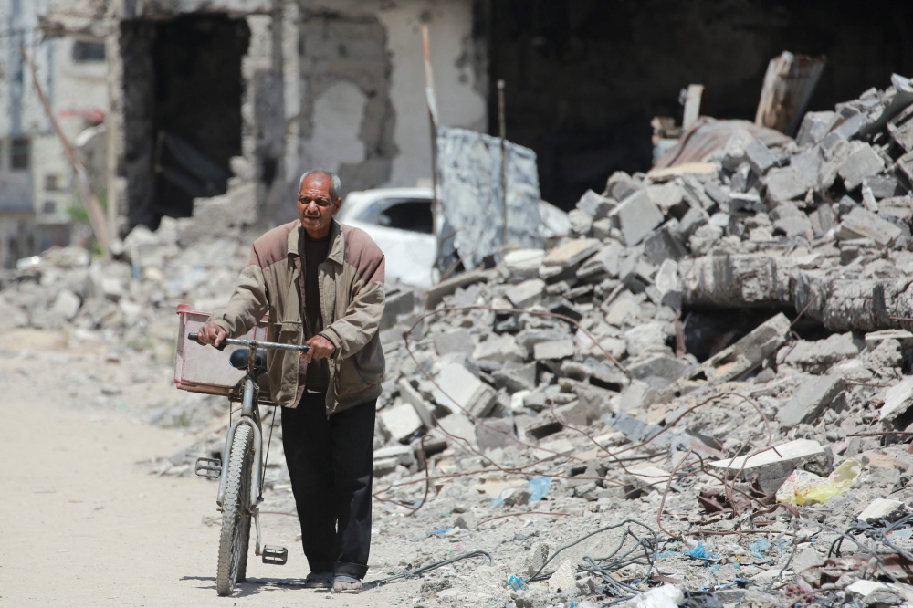 An elderly Palestinian man pushes a bicycle past the rubble of destroyed buildings in Gaza City,