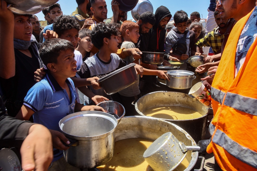 Palestinians line up to receive a hot meal at a food distribution point in the Al-Rimal neighbourhood. — AFP