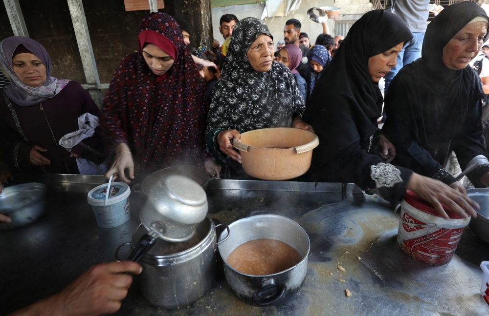 Palestinians wait to receive food cooked by a charity kitchen, in Gaza. — Reuters