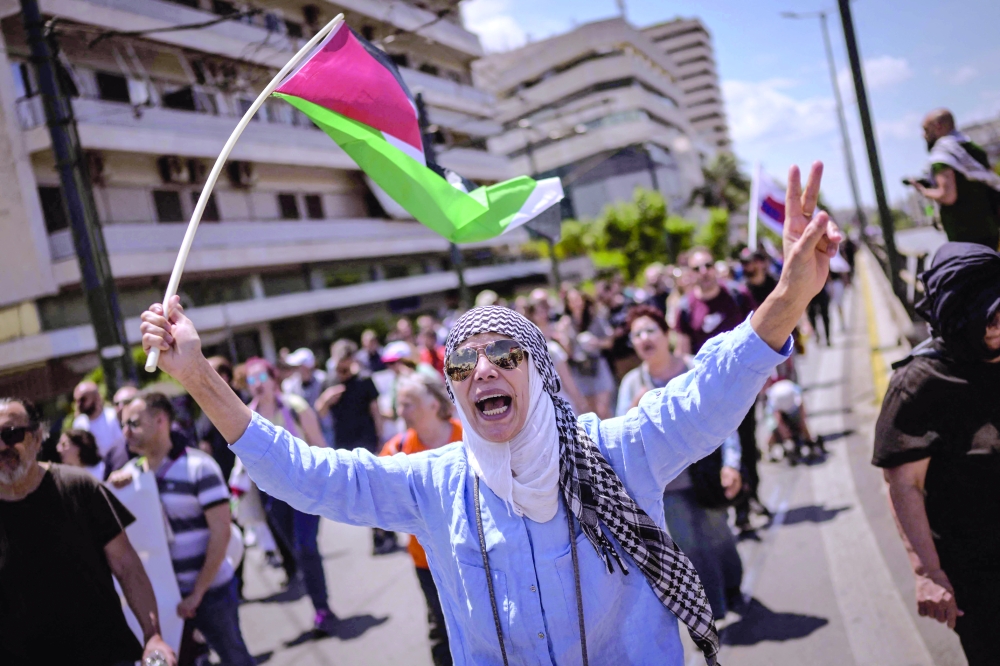 A protester holds a Palestinian flag and makes a peace symbol with her fingers as she marches with others to the Israeli embassy to demand freedom for Palestine, in Athens on Saturday. — AFP