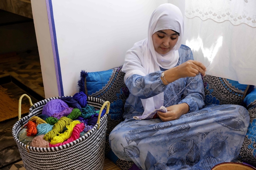 A woman participates in an embroidery workshop in Sidi Rbat, some 70 kilometres (45 miles) south of Agadir, on May 14, 2025. French Morocco artist Margaux Derhy founded the workshop in 2022 in her father's native village of Sidi R'bat, to fulfil her "dream to make art with purpose". The project uses textile and old photographs to explore her family heritage before they left the country in the 1960s, turning sepia-toned portraits and scenes into large silk-and-linen canvases. Just 19 percent of Moroccan women hold steady jobs, according to official figures, and in rural areas they are particularly affected by poverty, unpaid labour and a lack of opportunity.
 (Photo by Abdel Majid BZIOUAT / AFP)

