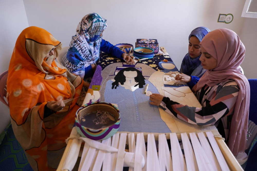 Women attend an embroidery workshop in Sidi Rbat, some 70 kilometres (45 miles) south of Agadir, on May 14, 2025. French Morocco artist Margaux Derhy founded the workshop in 2022 in her father's native village of Sidi R'bat, to fulfil her "dream to make art with purpose". The project uses textile and old photographs to explore her family heritage before they left the country in the 1960s, turning sepia-toned portraits and scenes into large silk-and-linen canvases. Just 19 percent of Moroccan women hold steady jobs, according to official figures, and in rural areas they are particularly affected by poverty, unpaid labour and a lack of opportunity.
 (Photo by Abdel Majid BZIOUAT / AFP)

